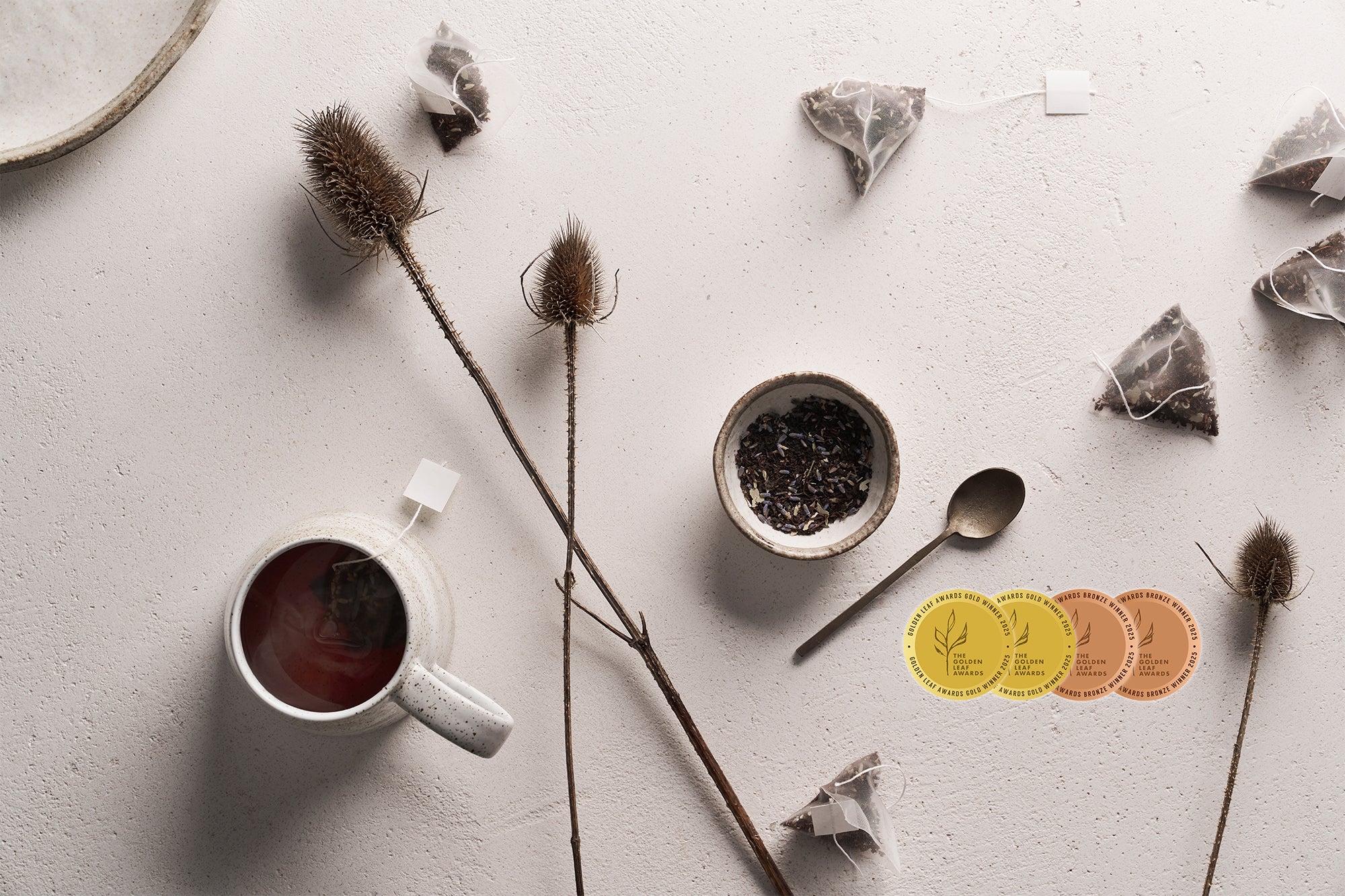 Tea cup with tea leaves, teabags, and a spoon on a light surface.